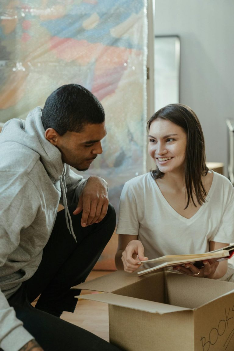 A cheerful couple unpacks books while moving into their new apartment, showing the excitement of a fresh start.